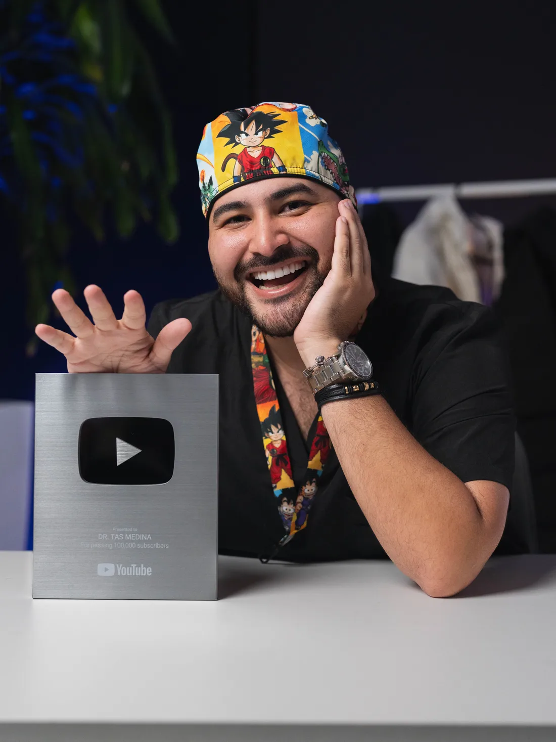 Dr. Tas Medina sonriendo junto a su placa de 100.000 suscriptores de YouTube